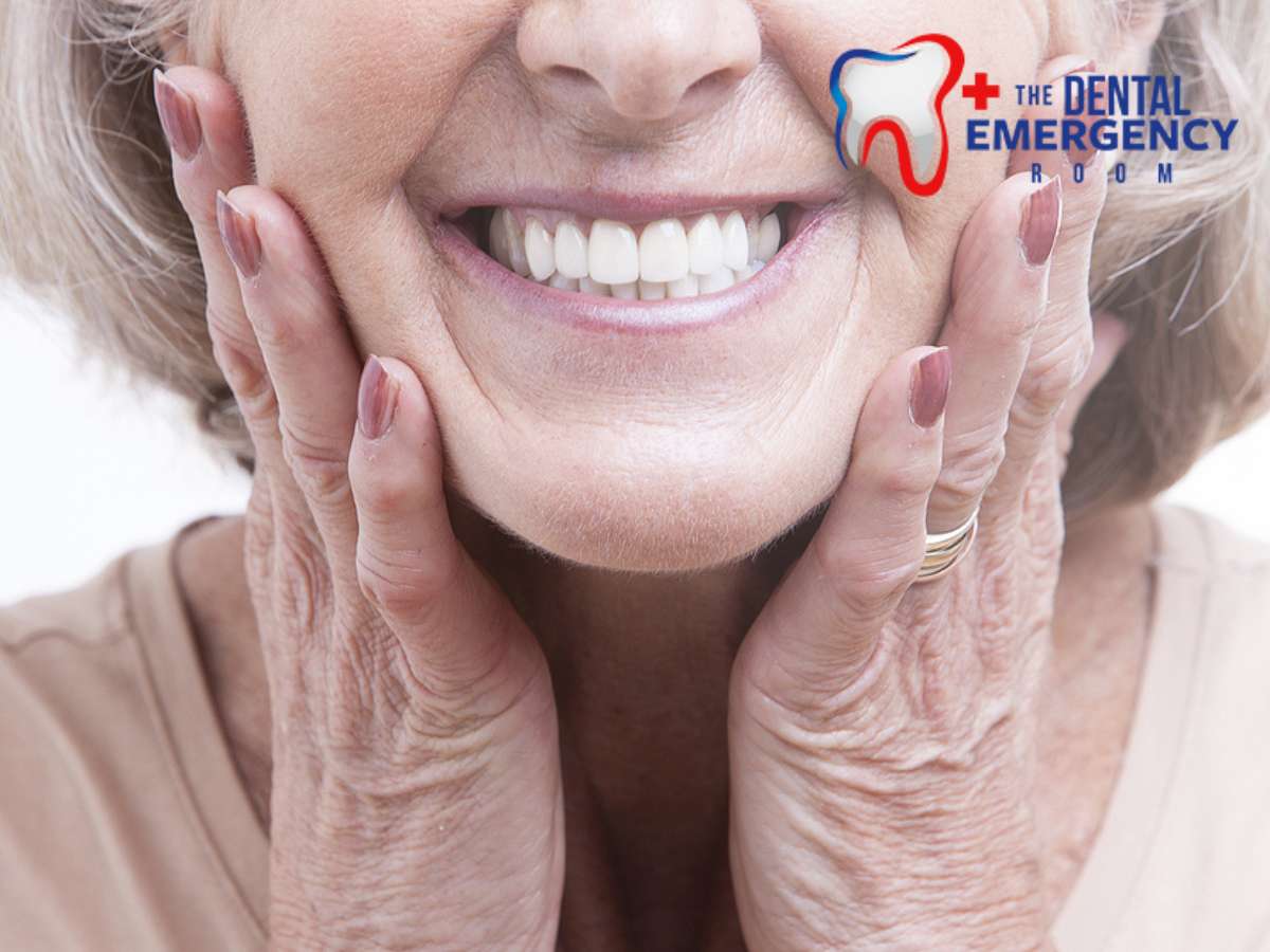 Elderly woman smiling and touching her cheeks, showcasing her new dentures with The Dental Emergency Room logo in the corner